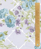 Floral fabric pattern with large light blue flowers, smaller lavender-purple blossoms, and green leaves over a pale lavender background with a white trellis design. A wooden ruler is shown vertically on the right side for scale.