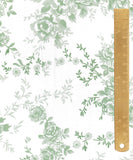 White fabric with a green floral toile pattern, shown flat with a wooden ruler on the right side for scale.