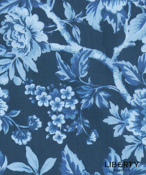 A close-up of Liberty Fabrics floral patterned fabric featuring light blue and white flowers and leaves on a dark navy blue background.