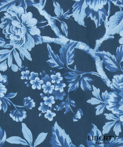 A close-up of Liberty Fabrics floral patterned fabric featuring light blue and white flowers and leaves on a dark navy blue background.