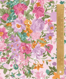 A close-up of a floral fabric pattern with pink, purple, orange, and teal flowers on a pale pink background, with a gold metal ruler standing vertically along the right side for scale.
