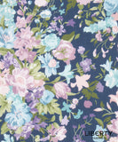 A close-up of Liberty Fabrics floral patterned fabric featuring pastel pink, light blue, and purple flowers with green leaves on a dark navy blue background.