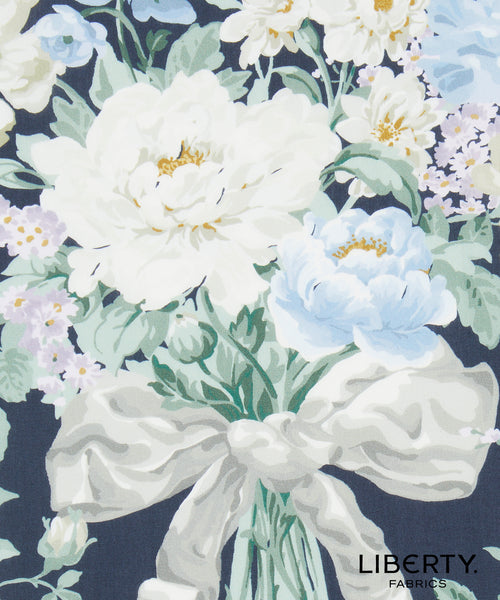 Liberty Fabrics floral fabric print featuring large white and light blue peonies with green leaves and stems on a dark navy background, with the Liberty Fabrics logo in the bottom right corner.