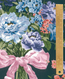 A close-up of a floral fabric or wallpaper pattern featuring large light blue and lavender peonies with a pink ribbon, green leaves, and small pink flowers on a dark teal background, with a wooden ruler shown vertically on the right side for scale.