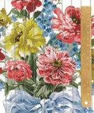 A close-up of a floral fabric print with large pink and yellow flowers, blue blossoms, green leaves, and a light blue bow, shown with a wooden ruler along the right edge for scale.