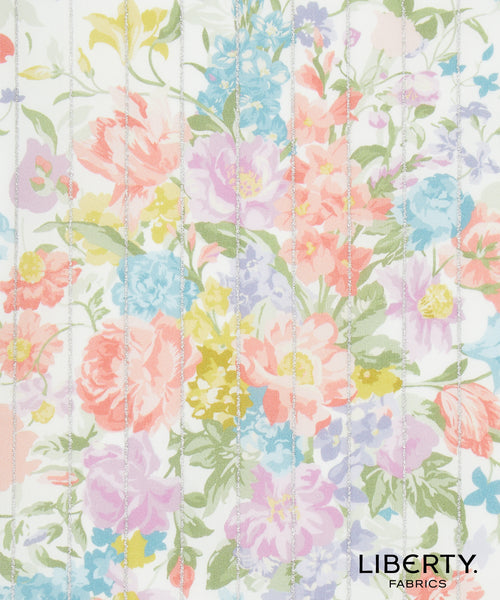A close-up of a floral fabric print with pastel pink, blue, yellow, and lavender flowers on a white background, overlaid with vertical quilting stitches. The brand name 'LIBERTY.